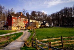 Boarding farm house in the sun with sidewalk next to grass and wooden fence